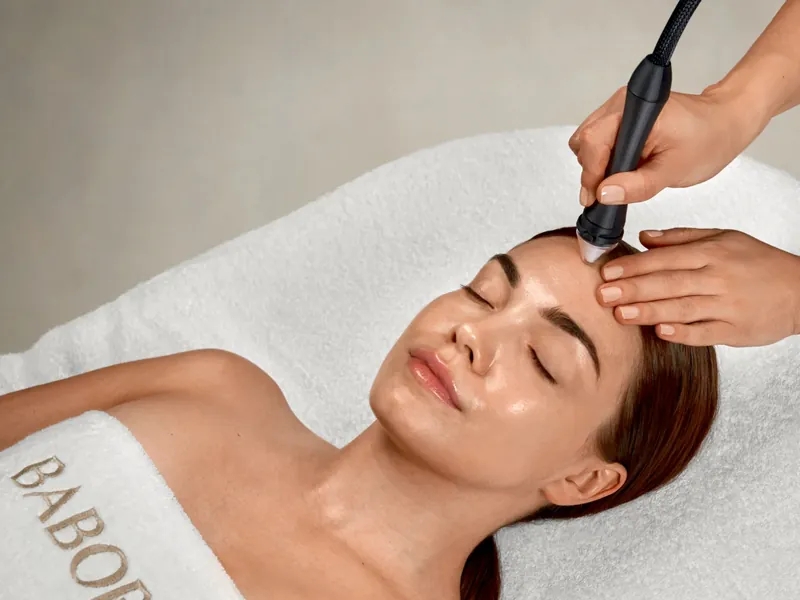 Kundin bei der Mikrodermabrasion, ein Handstück gleitet über die Stirn