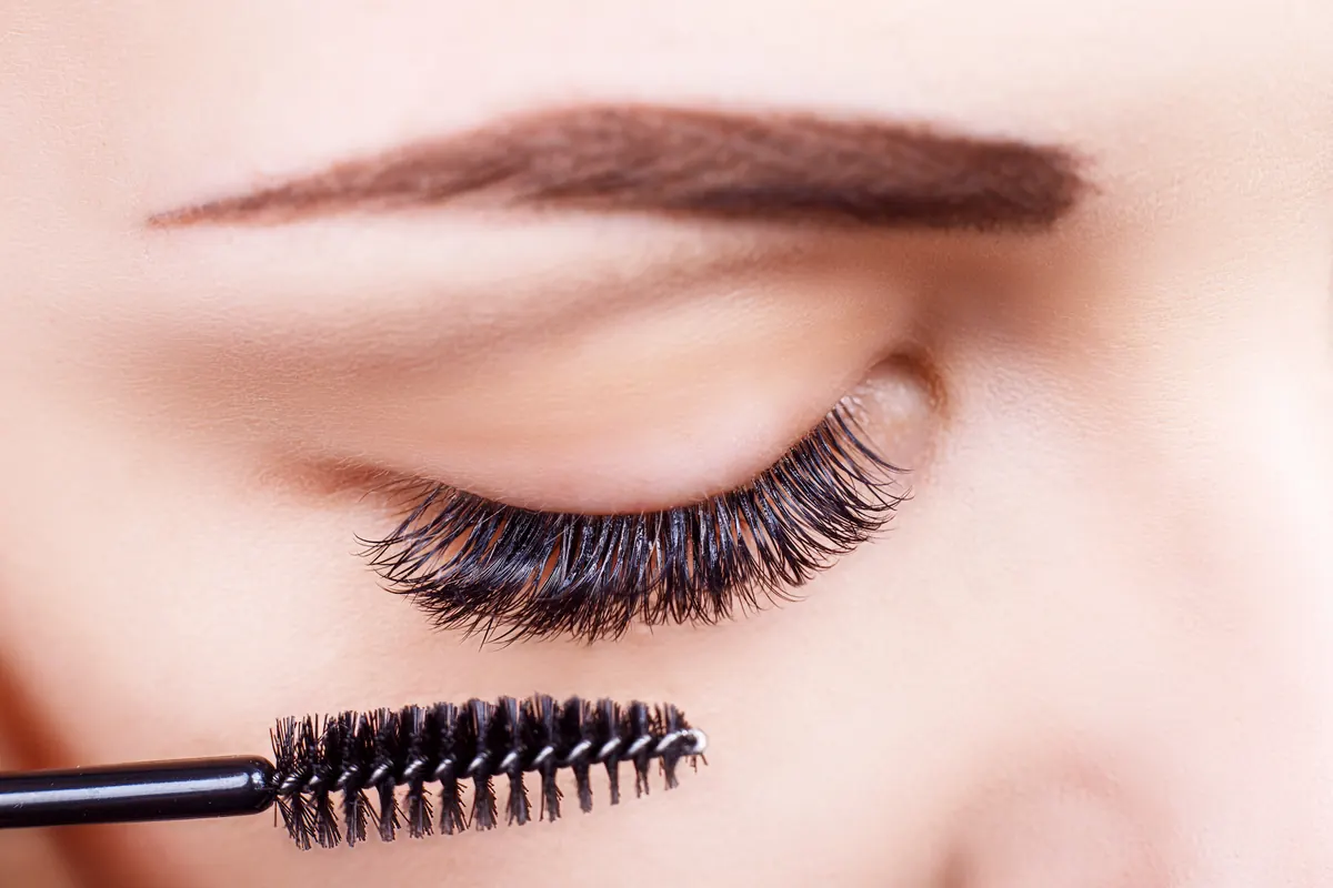 Nahaufnahme eines geschlossenen Auges mit dunklen Wimpern, darunter ein Wimpernbürstchen